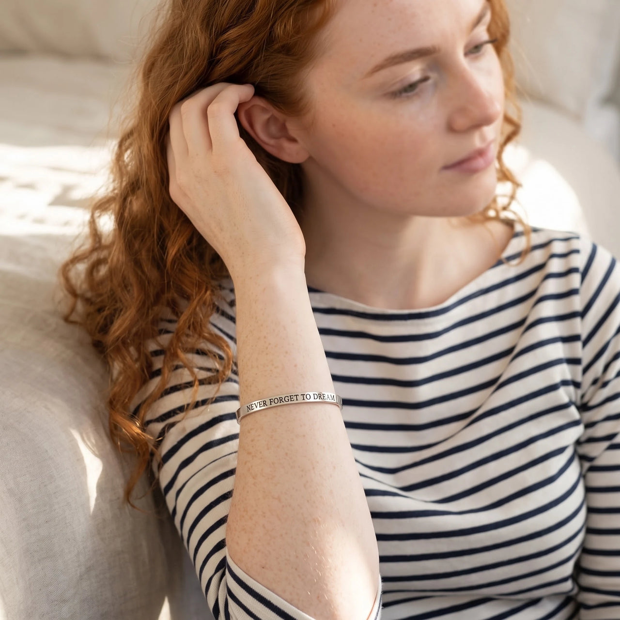 Woman gently touching her Never Forget To Dream bracelet in silver | SKU: nftd-wg